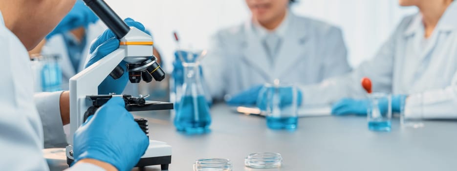 Group of dedicated scientist conduct chemical experiment using microscope in medical laboratory to develop new vaccine drug or antibiotic. Biotechnology lab and medicine research concept. Neoteric