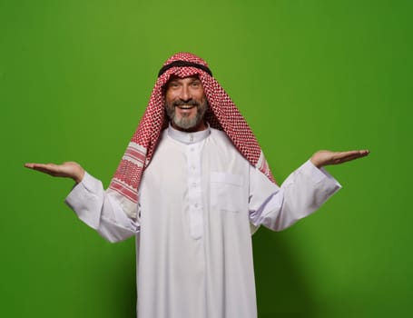 Muslim man holds two hands in gesture against green background, with empty blank copy space for text. Concept of choice and decision-making, man's contentment reflects satisfaction of making decision. High quality photo