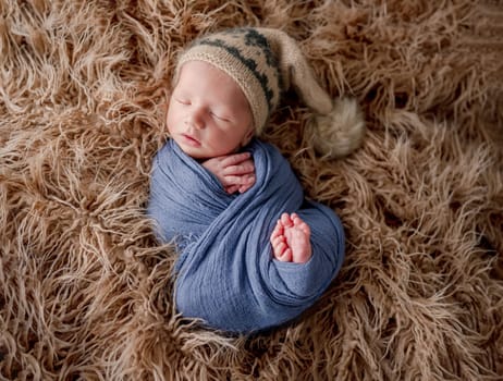 Adorable newborn baby boy smiling during sleeping and holding knitted giraffe toy. Cute infant child kid napping on fur