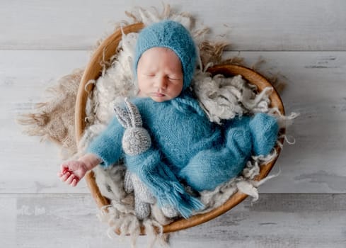 Adorable newborn baby boy sleeping holding knitted bunny toy in heart shape basket studio portrait. Cute infant child kid napping