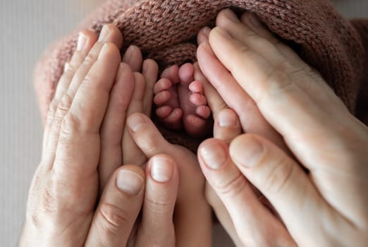Newborn baby tiny feet in parents hands family portrait. Mother and father care with love holding cute infant child kid legs