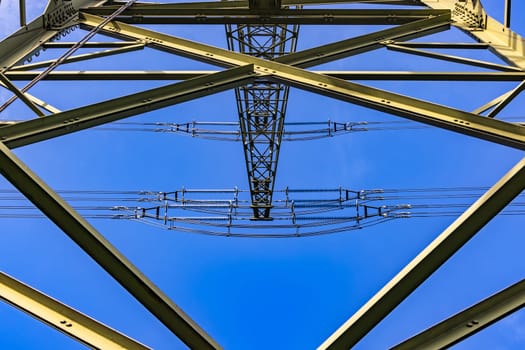 Struts and crossbeams from the steel skeleton of a power pole seen from below against the blue sky