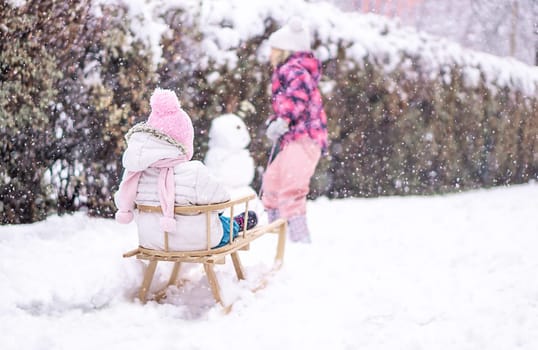 Girl sledding her sister in snow park. Family vacation in winter. High quality photo