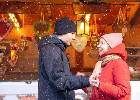 Young amorous couple smiling and keeping hands at the traditional Christmas market in Europe. High quality photo