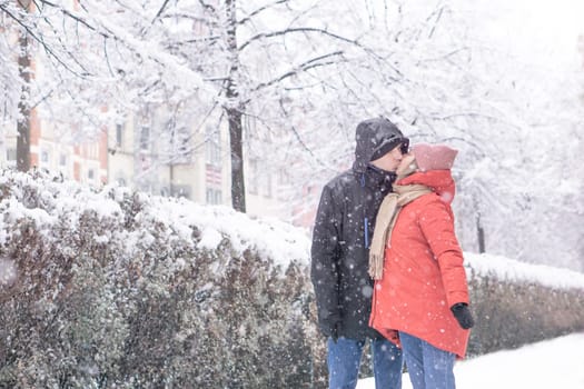 Happy amorous couple hugging each other and kissing at snow day in winter park. High quality photo