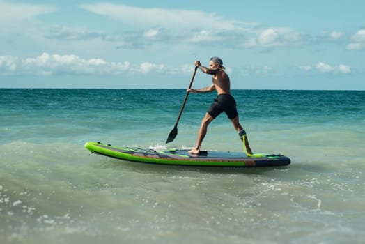 athletic wiry surfer guy swims with a paddle on a sup board in the sea