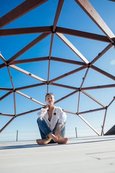 a woman sits on the floor under a wooden frame blue sky