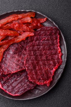 Dried beef slices, jerky, with cherry or plum flavor, salt and spices on a dark concrete background