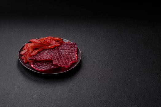 Dried beef slices, jerky, with cherry or plum flavor, salt and spices on a dark concrete background