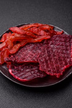 Dried beef slices, jerky, with cherry or plum flavor, salt and spices on a dark concrete background