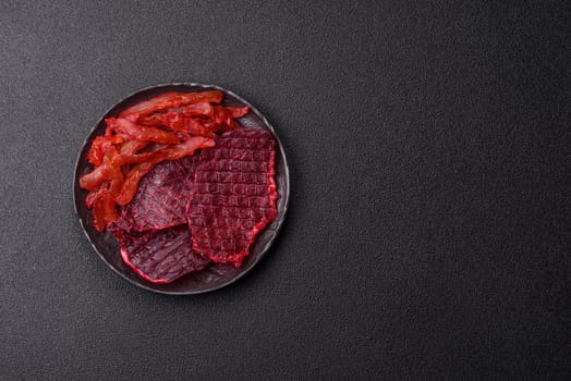 Dried beef slices, jerky, with cherry or plum flavor, salt and spices on a dark concrete background