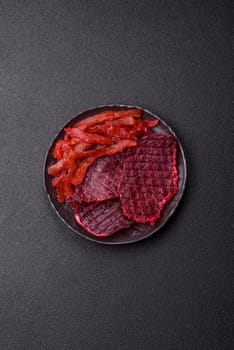 Dried beef slices, jerky, with cherry or plum flavor, salt and spices on a dark concrete background