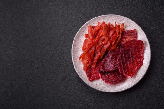 Dried beef slices, jerky, with cherry or plum flavor, salt and spices on a dark concrete background