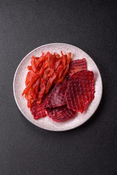 Dried beef slices, jerky, with cherry or plum flavor, salt and spices on a dark concrete background
