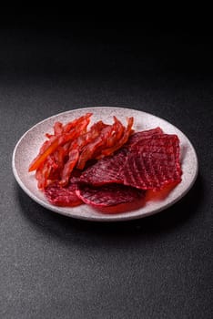Dried beef slices, jerky, with cherry or plum flavor, salt and spices on a dark concrete background