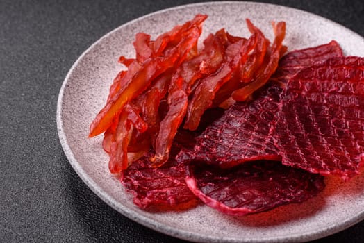 Dried beef slices, jerky, with cherry or plum flavor, salt and spices on a dark concrete background