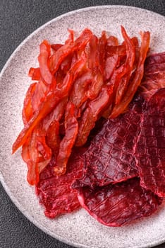 Dried beef slices, jerky, with cherry or plum flavor, salt and spices on a dark concrete background