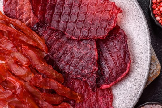 Dried beef slices, jerky, with cherry or plum flavor, salt and spices on a dark concrete background