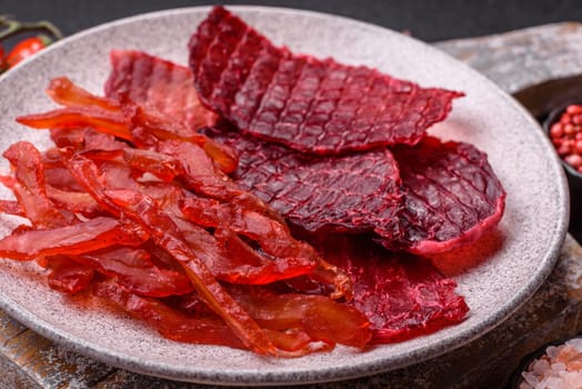 Dried beef slices, jerky, with cherry or plum flavor, salt and spices on a dark concrete background