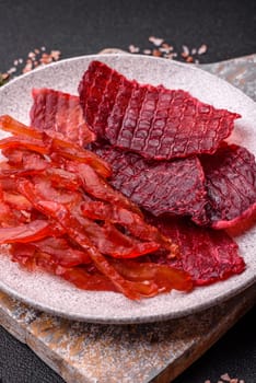 Dried beef slices, jerky, with cherry or plum flavor, salt and spices on a dark concrete background