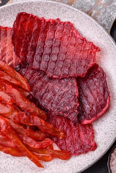 Dried beef slices, jerky, with cherry or plum flavor, salt and spices on a dark concrete background