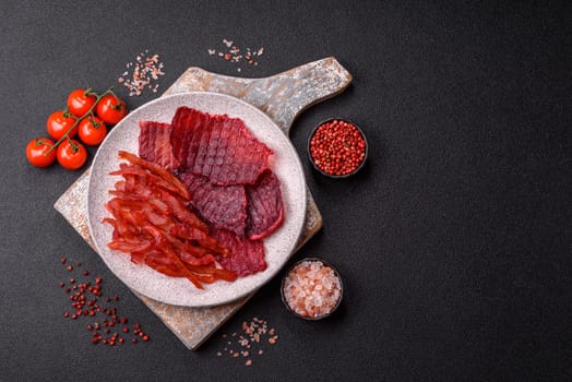 Dried beef slices, jerky, with cherry or plum flavor, salt and spices on a dark concrete background