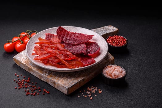 Dried beef slices, jerky, with cherry or plum flavor, salt and spices on a dark concrete background