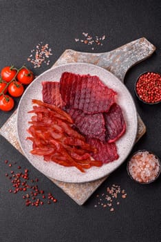 Dried beef slices, jerky, with cherry or plum flavor, salt and spices on a dark concrete background
