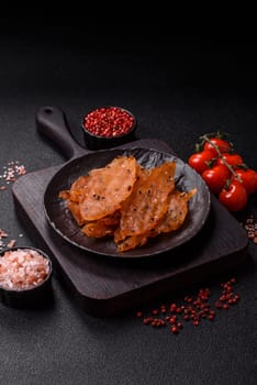 Jerky, dried chicken meat with salt and spices on a dark concrete background