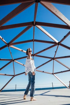 a woman stands under a wooden frame by the sea