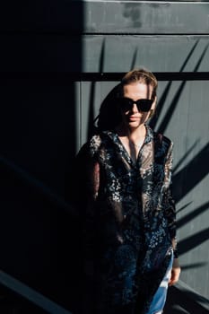 woman in sunglasses stands in the shade against a dark wall