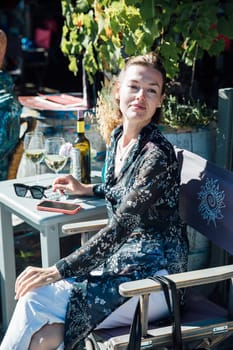 woman sits at a table in an outdoor restaurant on the street for two glasses of wine