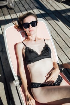 woman in a black swimsuit lies on a chaise longue on the beach rest