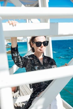 woman in sunglasses stands at the white stairs to the sea