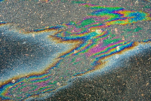 Spots of oil or gasoline are scattered randomly on the asphalt after rain. Abstract background close-up