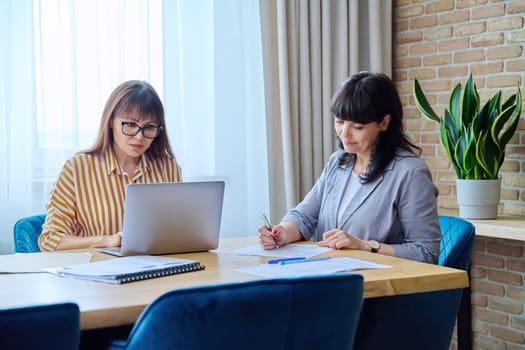 Two mature business women colleagues employees working together in office, middle-aged females preparing contract financial legal plan. Work professionals teamwork communication 40s 50s people on job