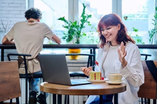 Female college student with laptop in cafeteria at table with cup of coffee and piece of cake. Internet online technology for leisure communication blogging learning chat, youth lifestyle concept