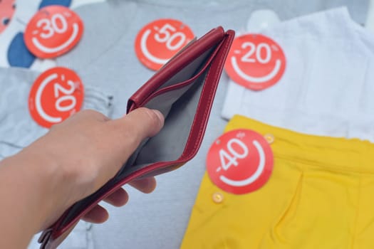 Female hands holding empty red purse background with clothes with discount labels