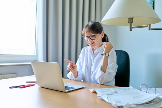 Mature business woman working remotely, having an online chat conference, in home office. Female manager accountant mentor teacher freelancer talking on video call on laptop computer with clients