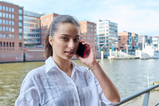 Young attractive teenage girl talking on mobile phone, outdoor on modern city. Teenager, college student communicating on smartphone. Urban style, communication, lifestyle, youth