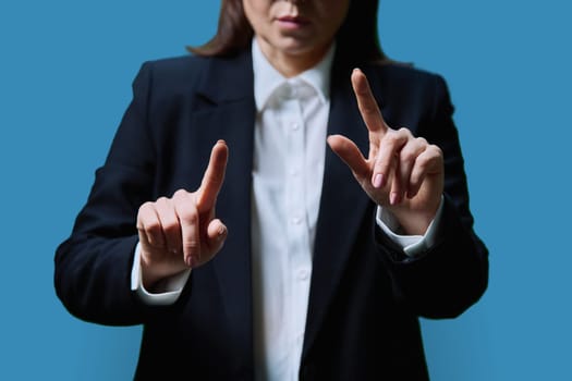 Close-up of business woman's hands using invisible touchscreen pressing key on virtual screen, on blue studio background. Business, work, profession, technology concept.