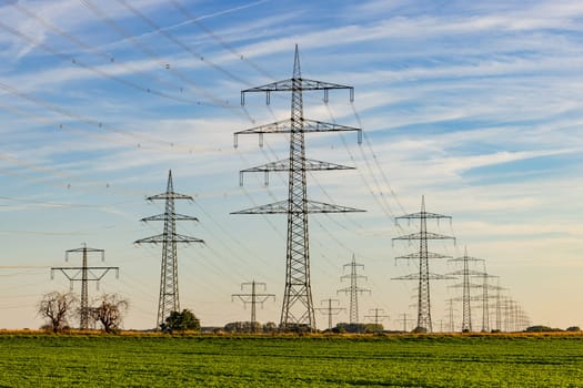 Countless artificially erected power poles and power lines in conflict with the natural environment at sunset, Germany