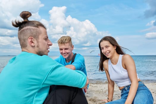 Friends teenagers laughing talking having fun sitting on the sand on the beach. Youth, adolescence, vacation, leisure, team, friendship, fun, lifestyle, summer holiday