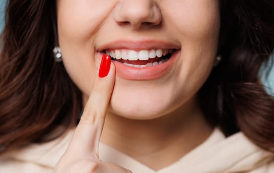 Happy girl showing toothy smile, pointing finger at healthy white teeth. Clinic patient satisfied with dentist service, enamel cleaning, whitening, dental care, correction. Cropped shot, close up. High quality photo