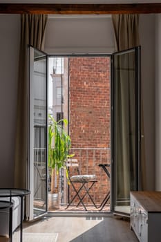 Open glass door of comfortable terrace with table and chair in renovated flat. Cosy place to rest on apartment balcony in Barcelona city