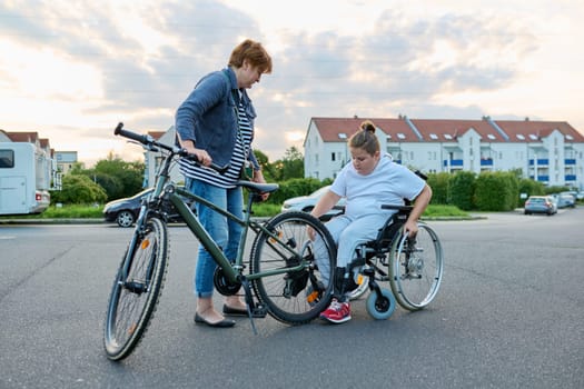 Boy transfers from wheelchair to bicycle, mother helping child to transfer, activity rehabilitation health concept