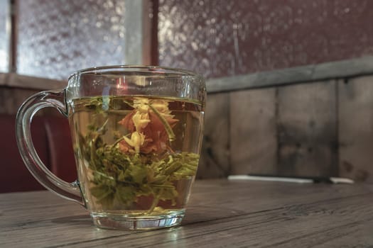 Glass cup with a tea flower in it. Flowering tea in glass cup on wooden teble, Healthy herbal drinks and natural healer concept, Space for text, Selective focus.