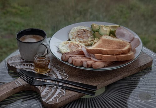 Breakfast is including Fried sausages, Fried eggs, Toast breads and cut avocados served with Honey and Cup of coffee. Oblique view from the top, Space for text, Selective focus.