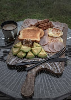 Breakfast is including Fried sausages, Fried eggs, Toast breads and cut avocados served with Honey and Cup of coffee. Oblique view from the top, Space for text, Selective focus.