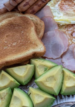 Close-up of Breakfast is including Fried sausages, Fried eggs, Toast breads and cut avocados. Space for text, Selective focus.